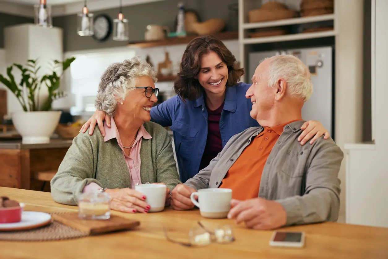 Happy smiling senior parents with adult daughter drinking tea how to talk to elderly parents about assisted living